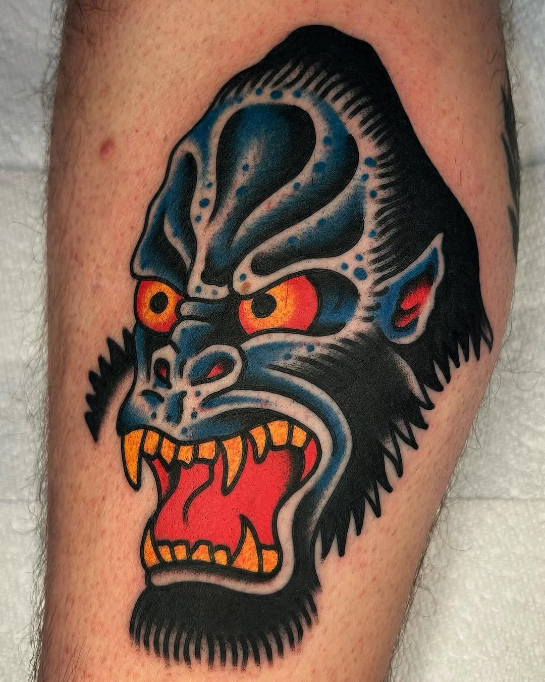 This tattoo features a striking image of a gorilla's face, capturing its fierce expression with bold black outlines and colors.
