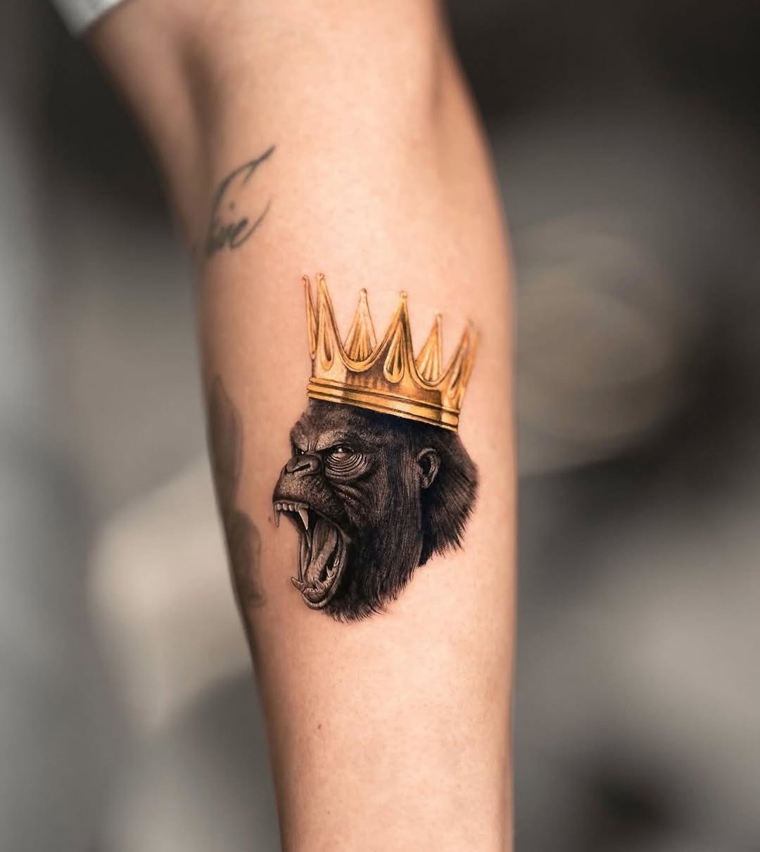 This striking tattoo features a powerful gorilla head, adorned with a golden crown.