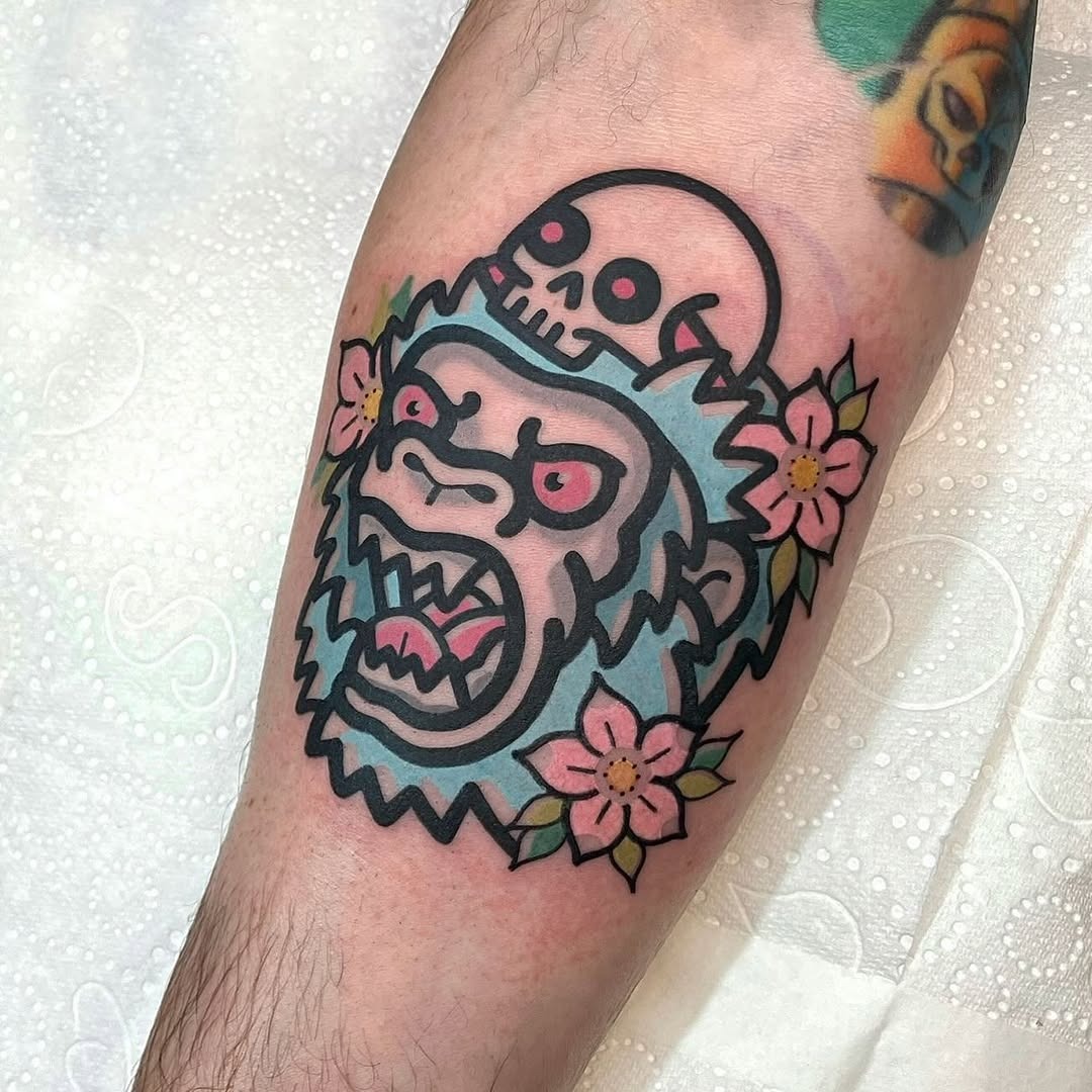 This tattoo showcases a striking gorilla with an expressive face, juxtaposed with a skull and blooming flowers.