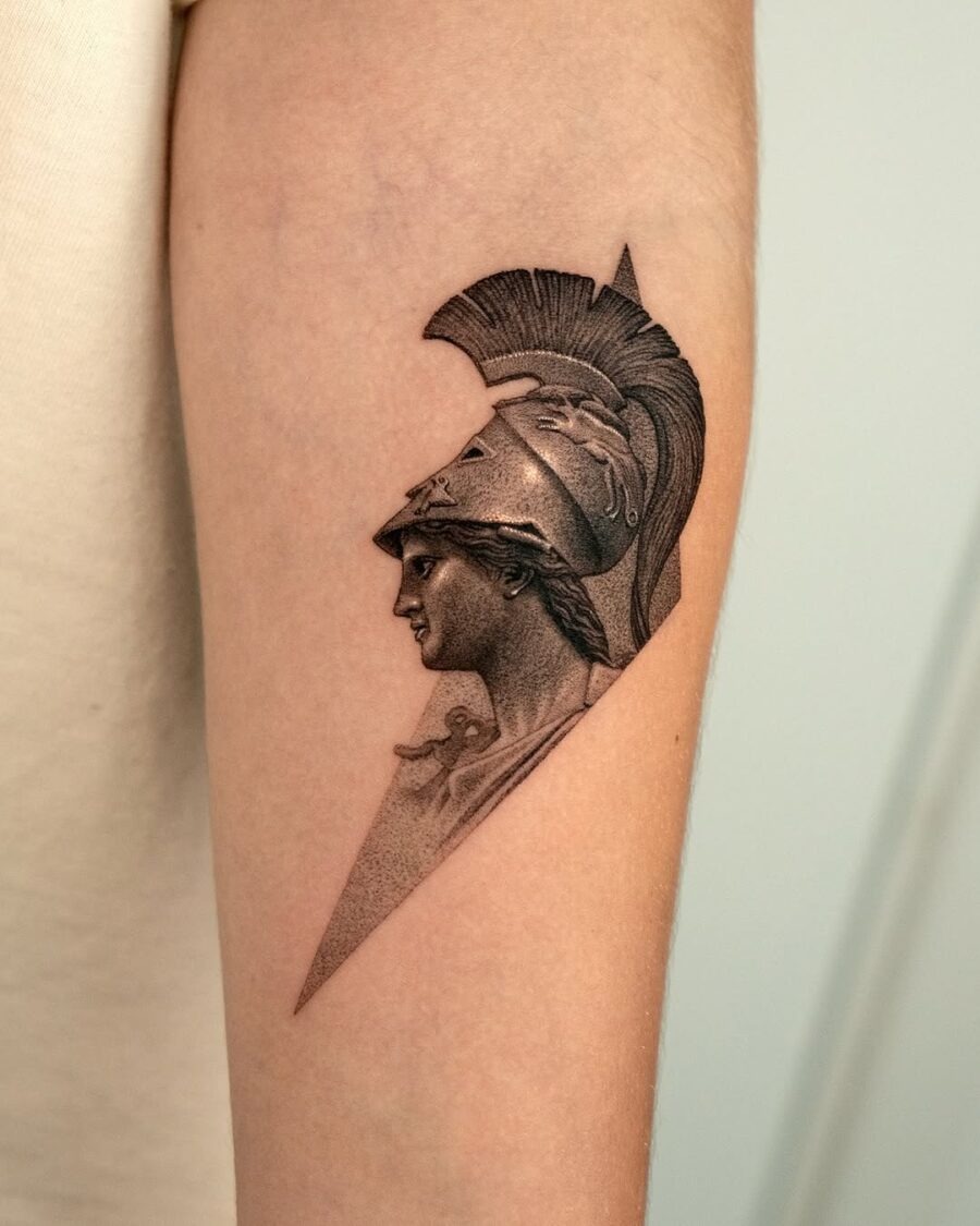 This striking tattoo captures the profile of Athena, depicted with her iconic helmet and a fierce expression.