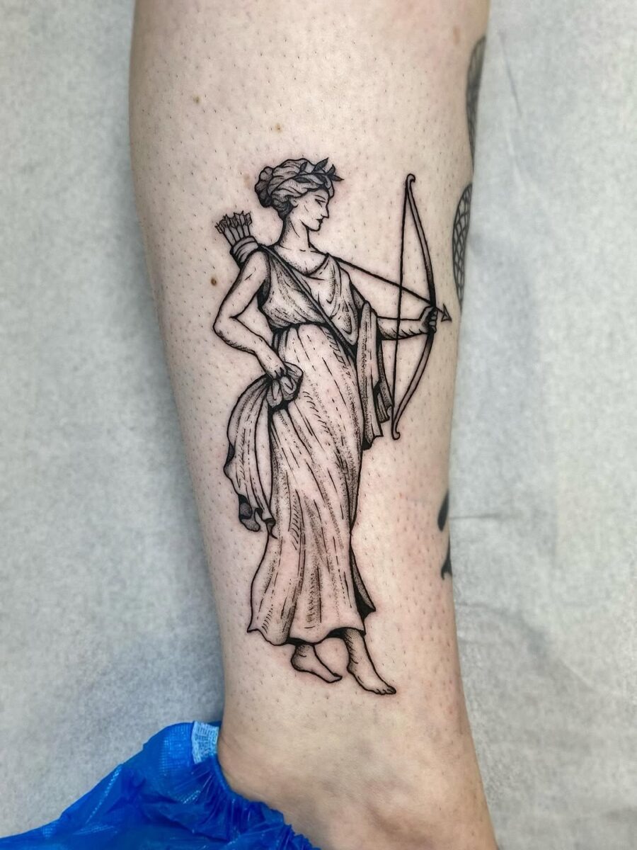 This tattoo depicts a graceful Greek goddess holding a bow, showing anatomical precision and flowing garments.