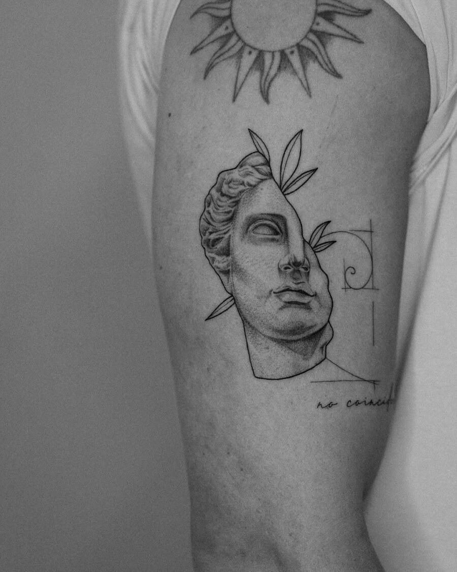This tattoo showcases a classical Greek god's bust, intricately designed with fine lines.