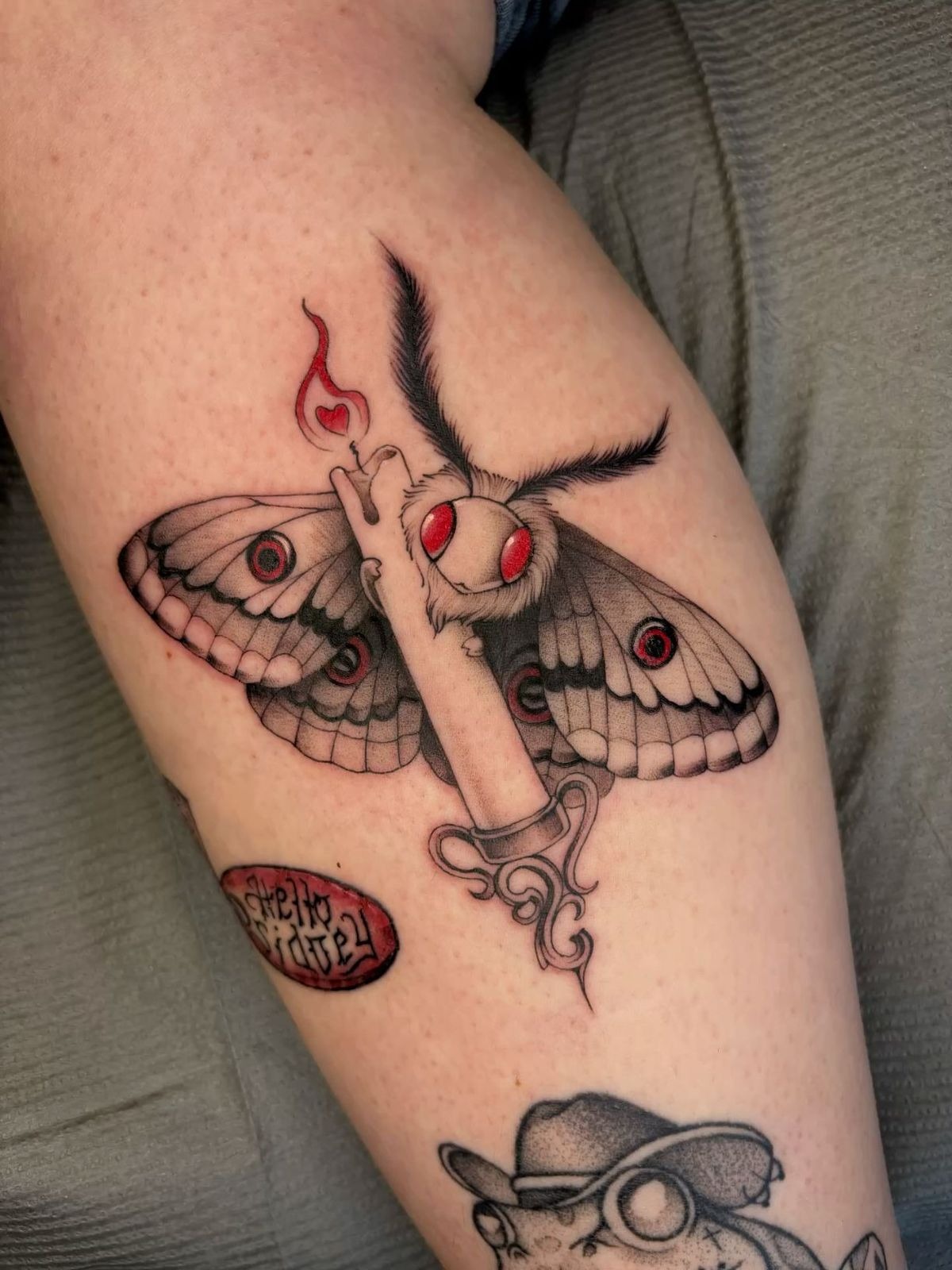 Moth with Candle and Red Eyes, a tattoo design rendered in clean detailed linework.