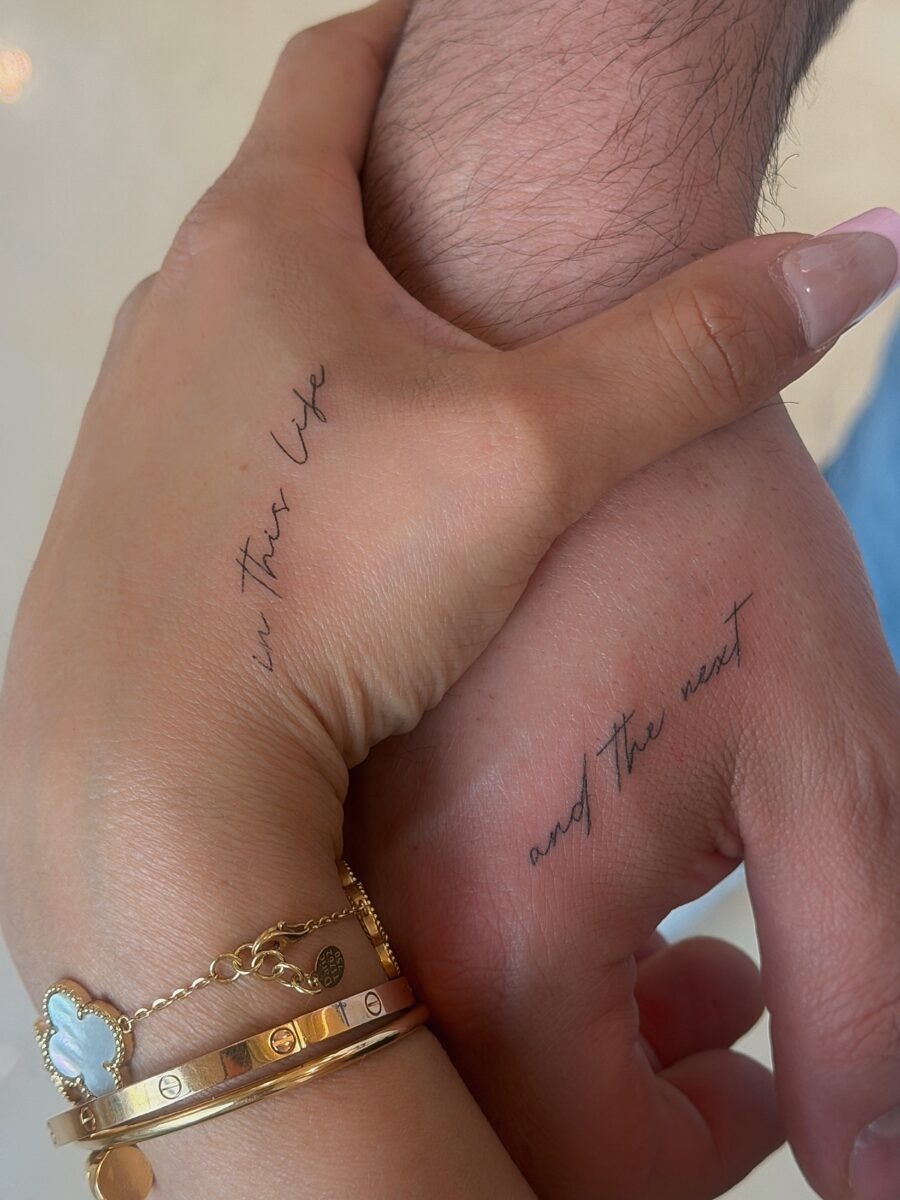 Delicate script tattoos on intertwined hands Tattoo Design