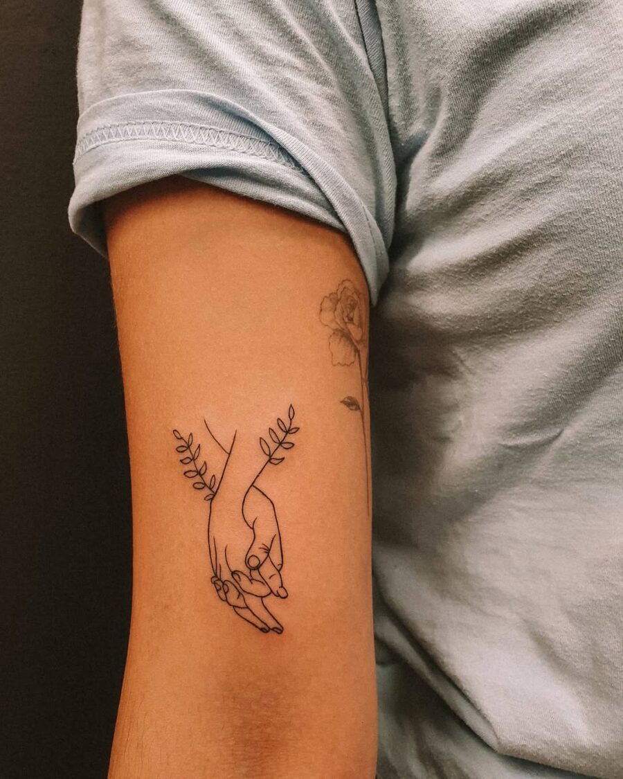 Delicate holding hands tattoo with floral accents Tattoo Design