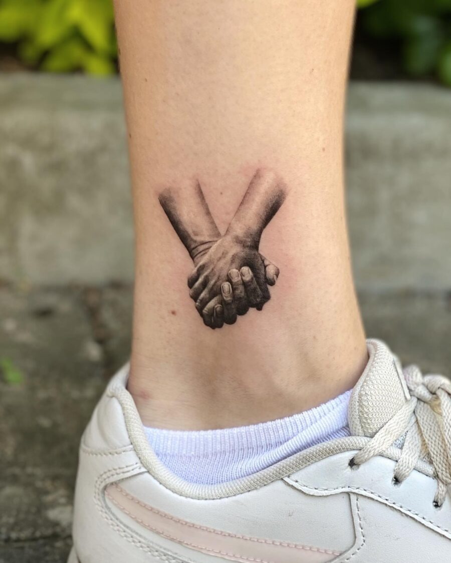 Intricate hand-holding tattoo on the ankle Tattoo Design