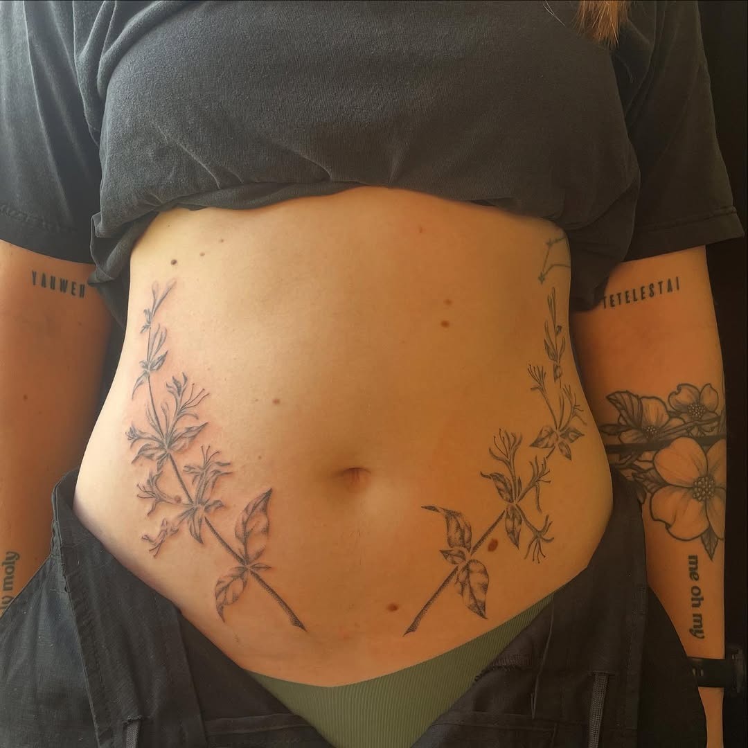 This stunning honeysuckle tattoo blooms gracefully on the stomach, showing intricate details and delicate lines.
