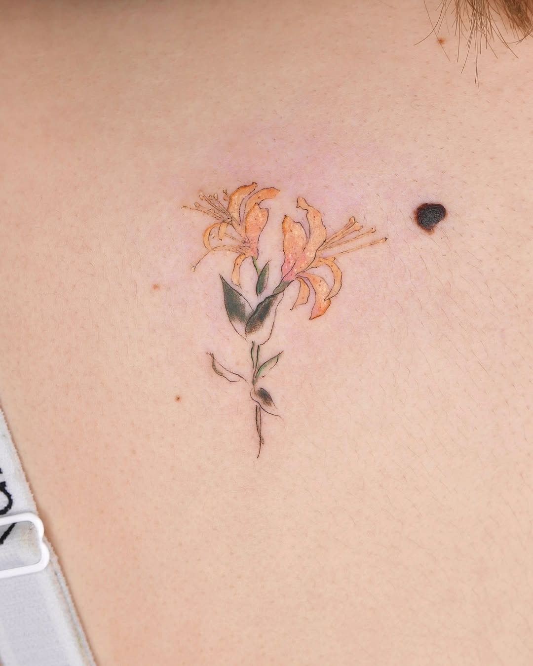 This delicate honeysuckle tattoo features bright orange blossoms and graceful green leaves.