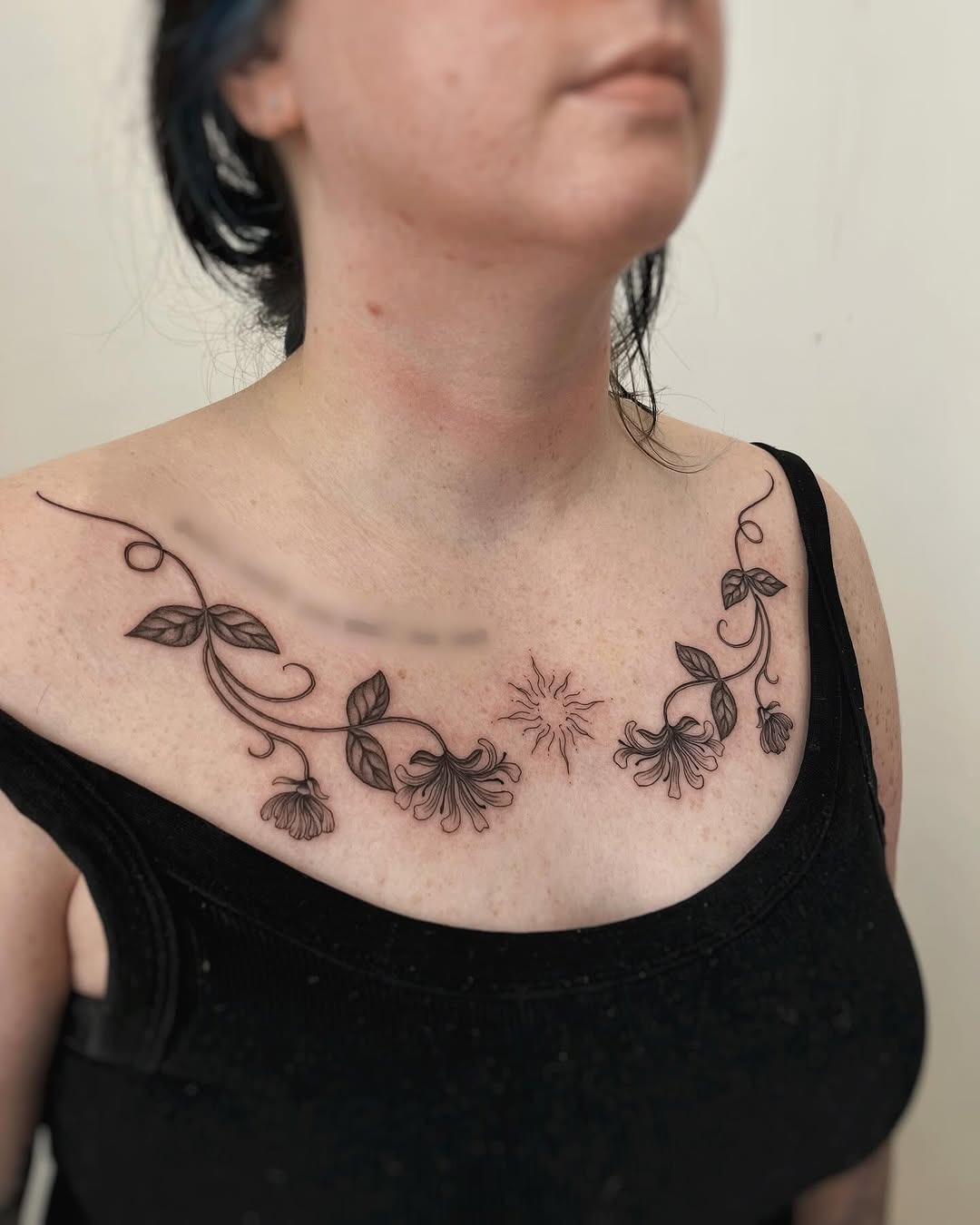 This honeysuckle tattoo beautifully drapes across the collarbone, showing intricate vine details.