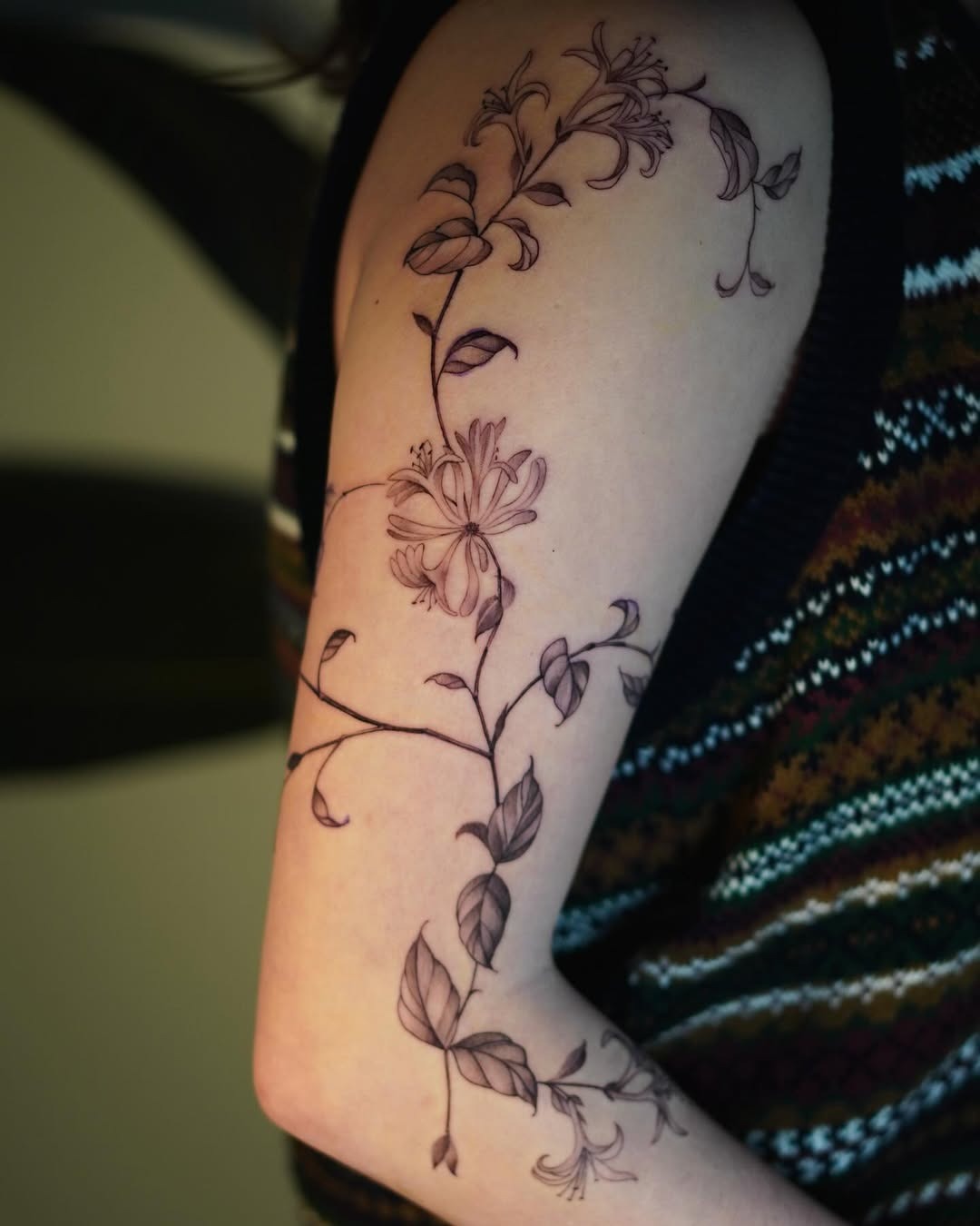This honeysuckle tattoo elegantly climbs the arm, showing intricate linework and soft floral details.