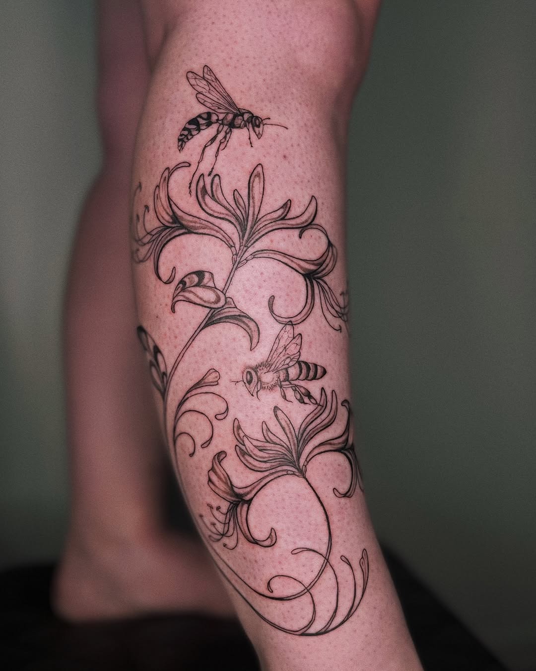 This stunning tattoo features a delicate honeysuckle vine intertwined with two buzzing bees, creating a sense of life and beauty.