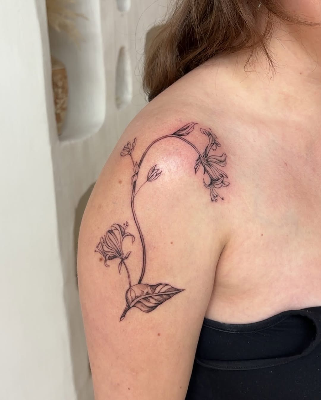 This honeysuckle tattoo features delicate linework and floral details, elegantly wrapping around the shoulder.