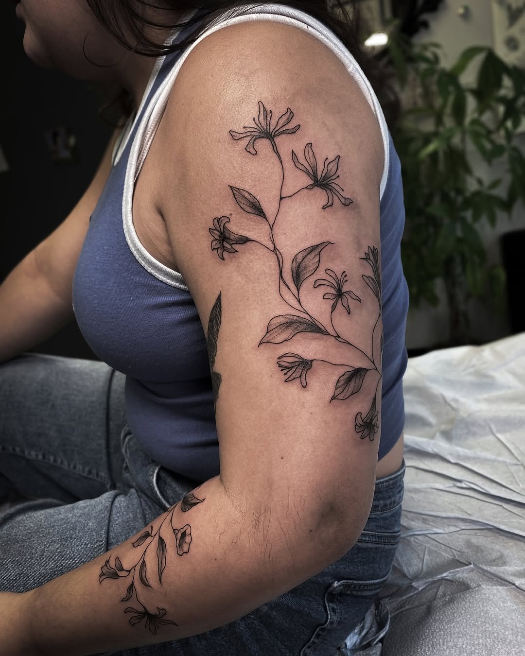 This stunning honeysuckle tattoo wraps elegantly around the arm, featuring delicate flowers and leaves.