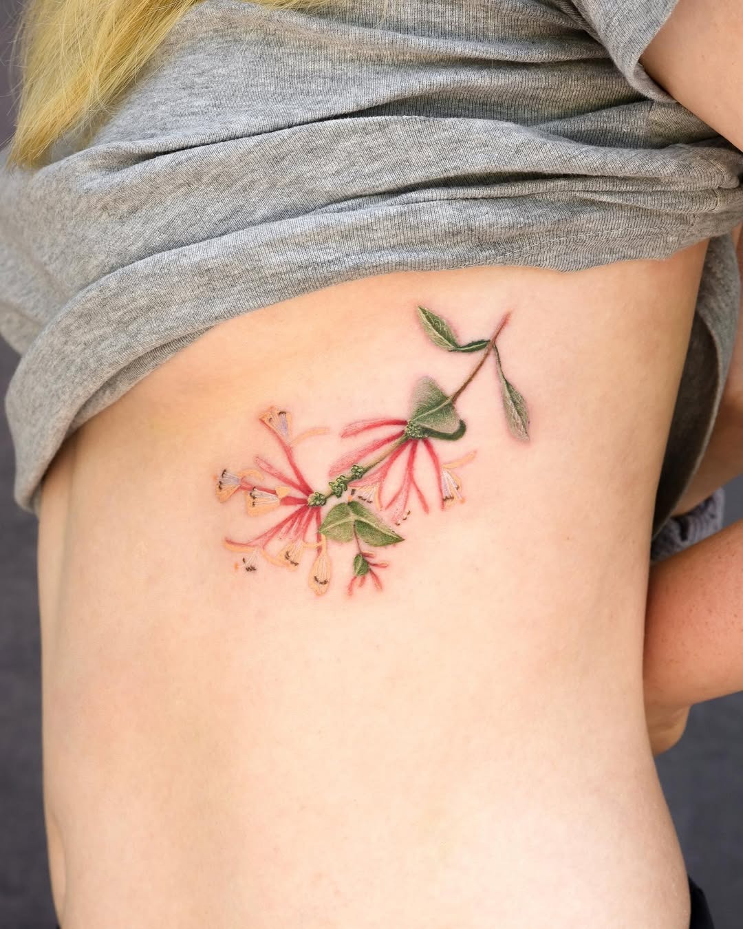 This gorgeous honeysuckle tattoo features pink and green colors, creating a lively floral design.