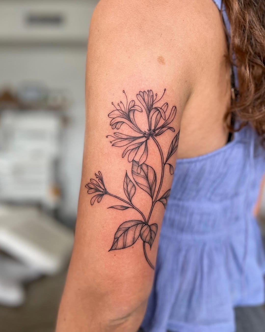 This honeysuckle tattoo features intricate black line art, wrapping gracefully around the arm.