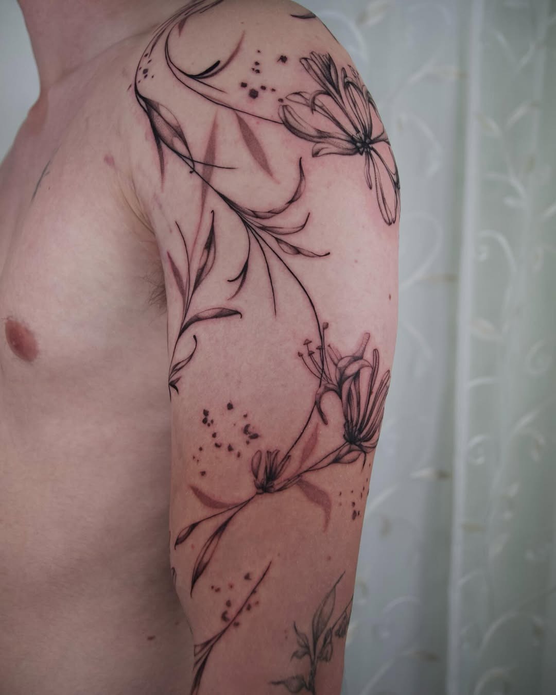 This tattoo showcases an intricate design featuring honeysuckle flowers entwined with elegant lines.