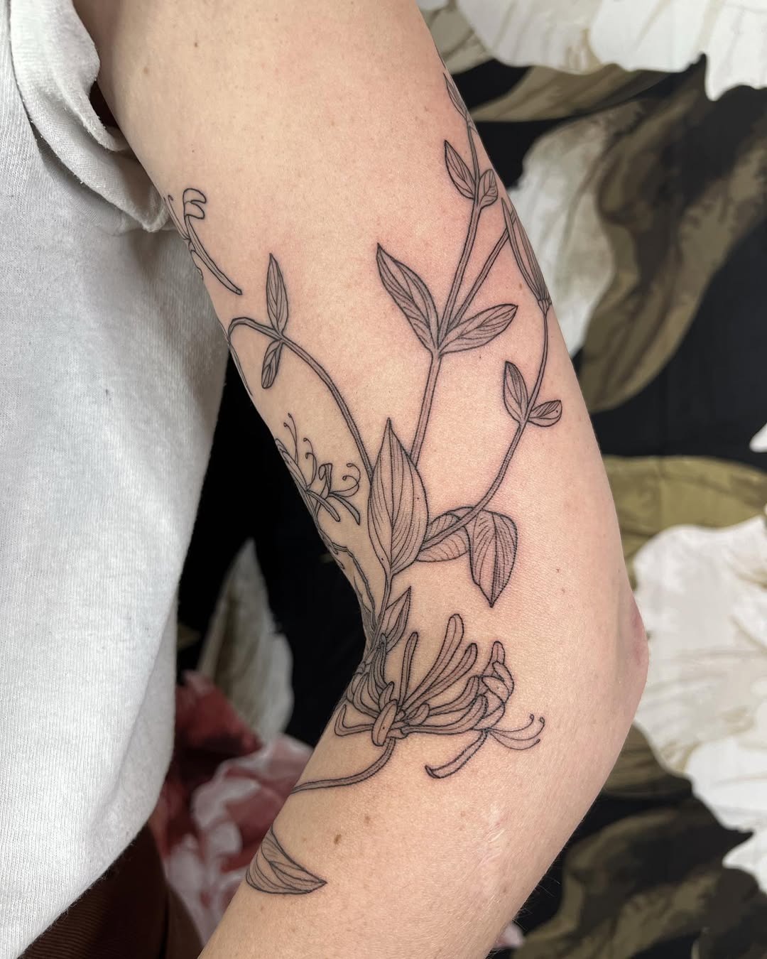 This honeysuckle tattoo features delicate fine line work, showing the beauty of the flower's intertwining vines.