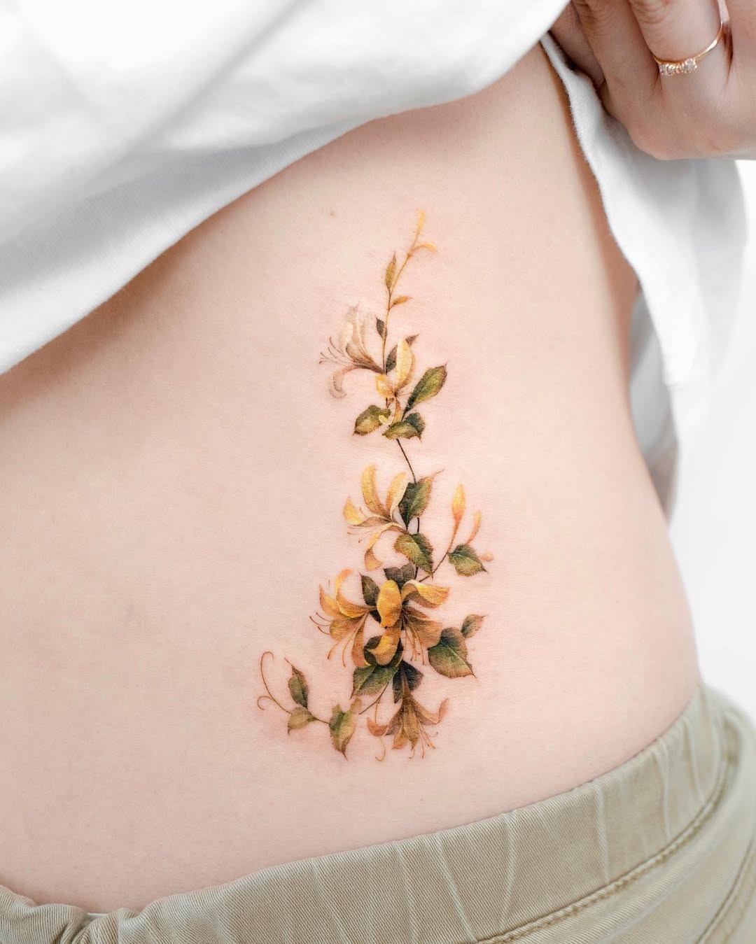 This beautiful honeysuckle tattoo gracefully winds along the rib cage, showing detailed floral artistry.