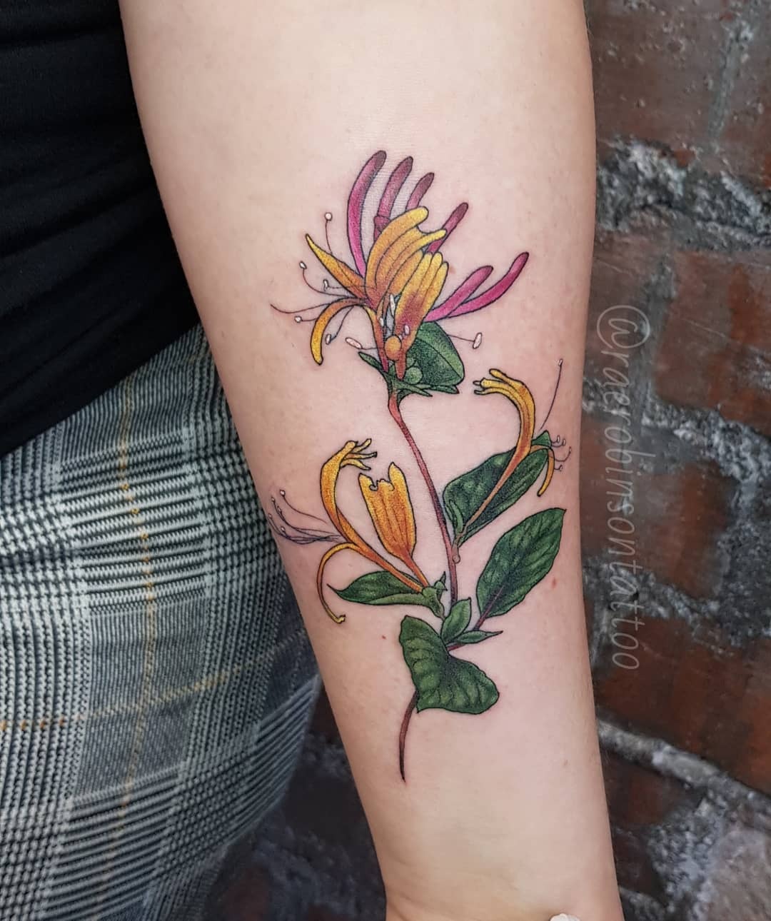 This honeysuckle tattoo features bright orange blooms and lush green leaves, capturing the essence of nature beautifully.