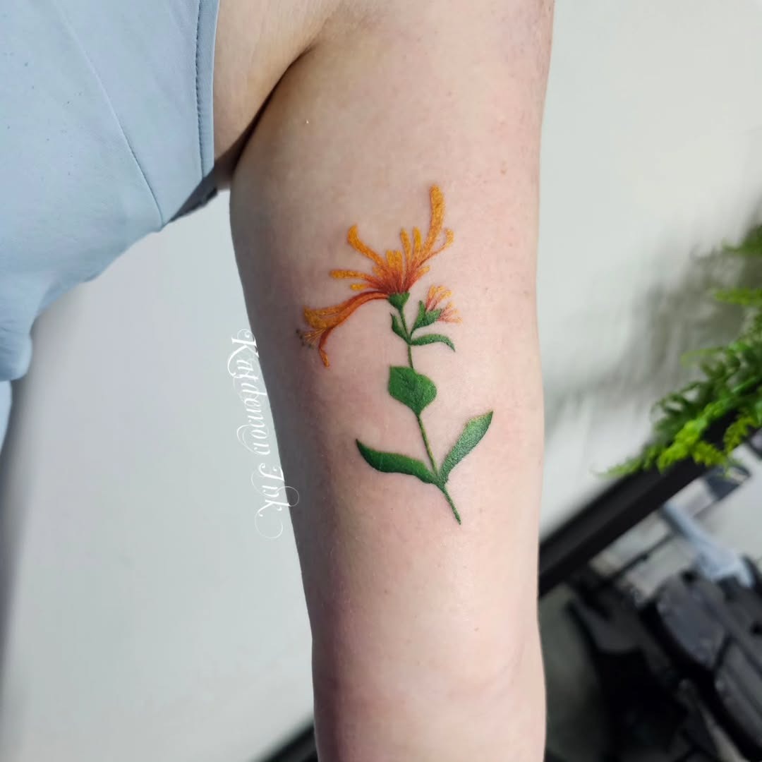This honeysuckle tattoo features bright orange blooms and lush green leaves, capturing the essence of nature beautifully.