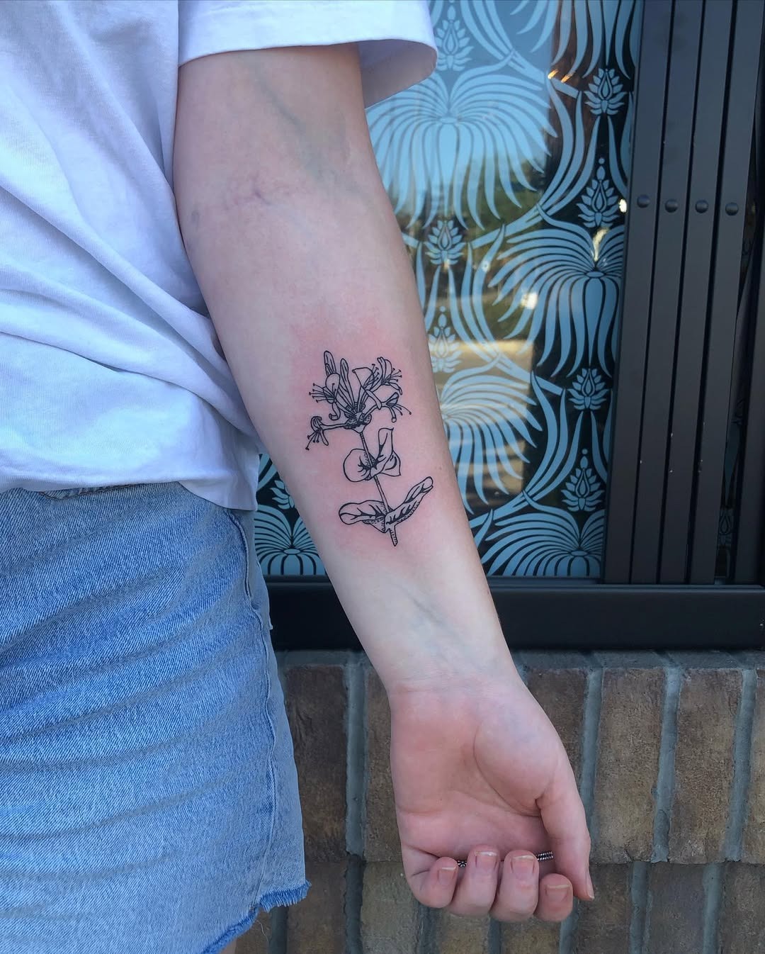 This honeysuckle tattoo features intricate black line art, elegantly wrapping around the arm.
