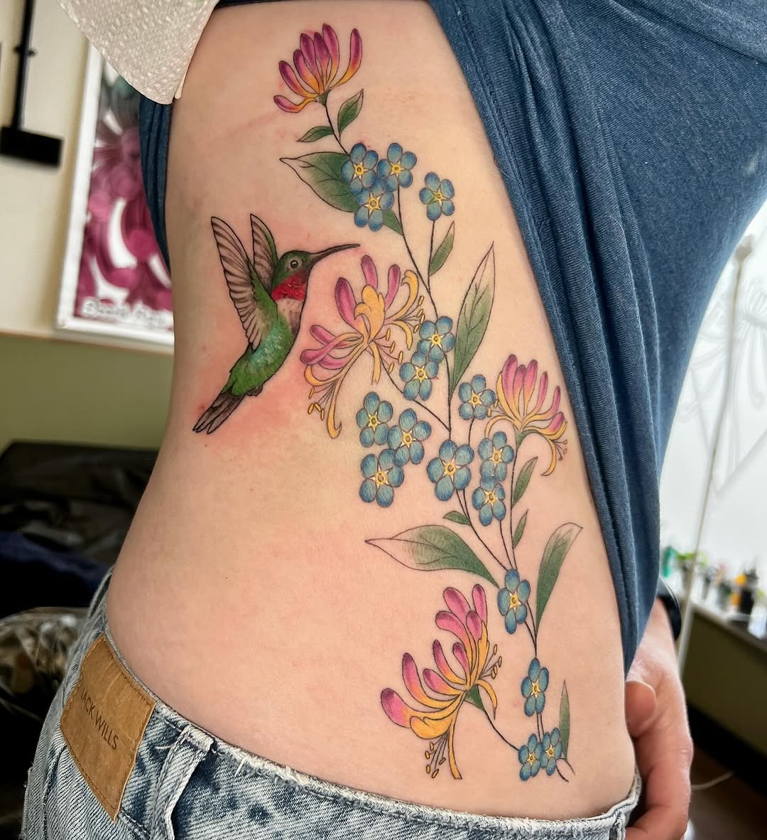 This stunning tattoo features a hummingbird hovering over honeysuckle flowers.