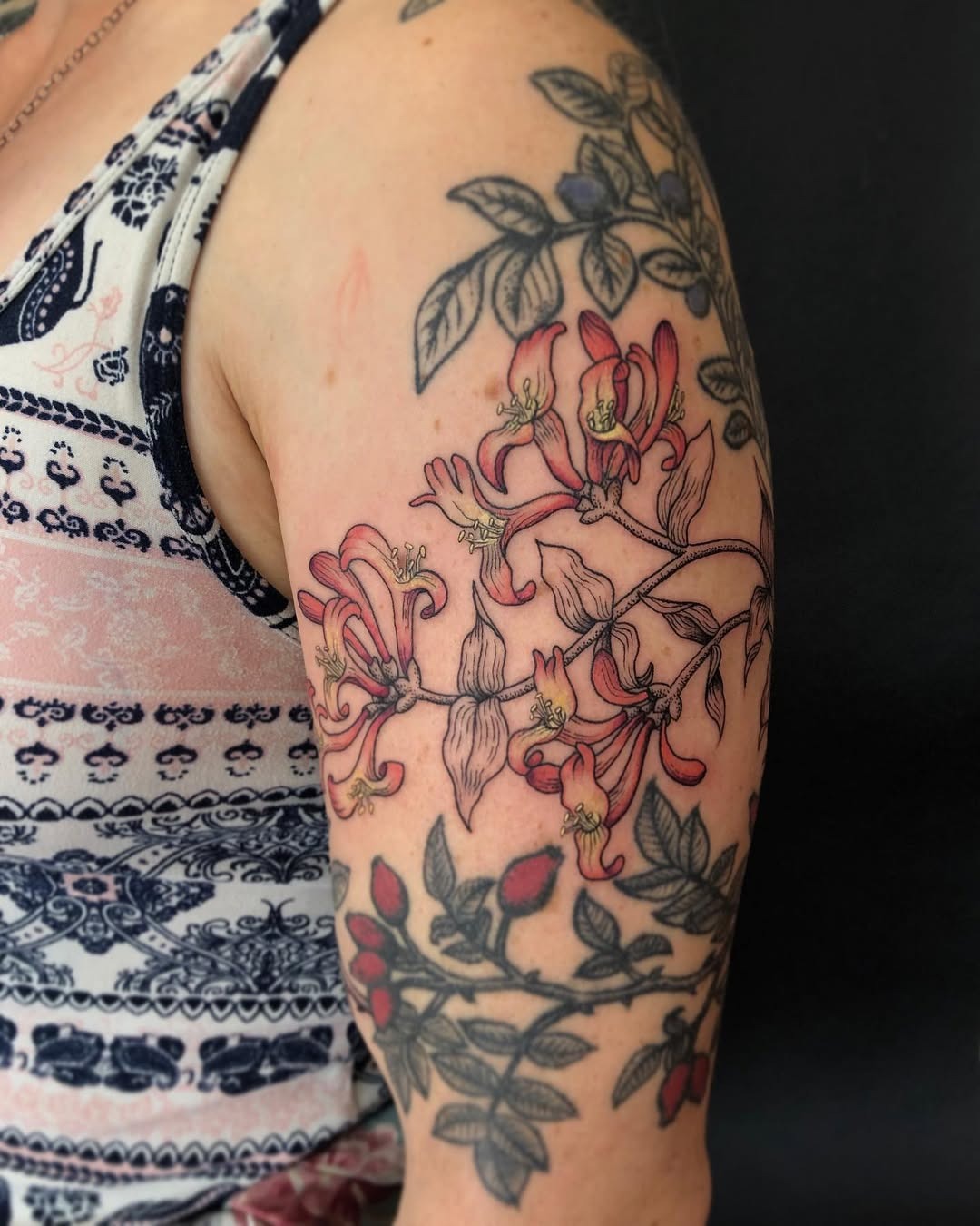 This honeysuckle tattoo showcases reds and delicate details intertwined among leaves.
