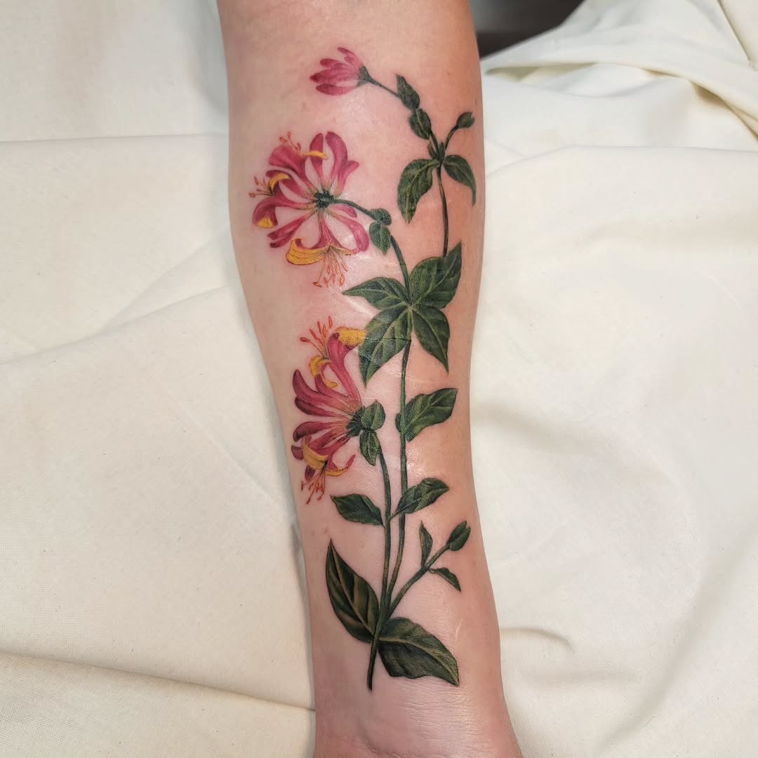 This honeysuckle tattoo features beautifully detailed flowers in pink and orange hues, accentuated by rich green leaves.