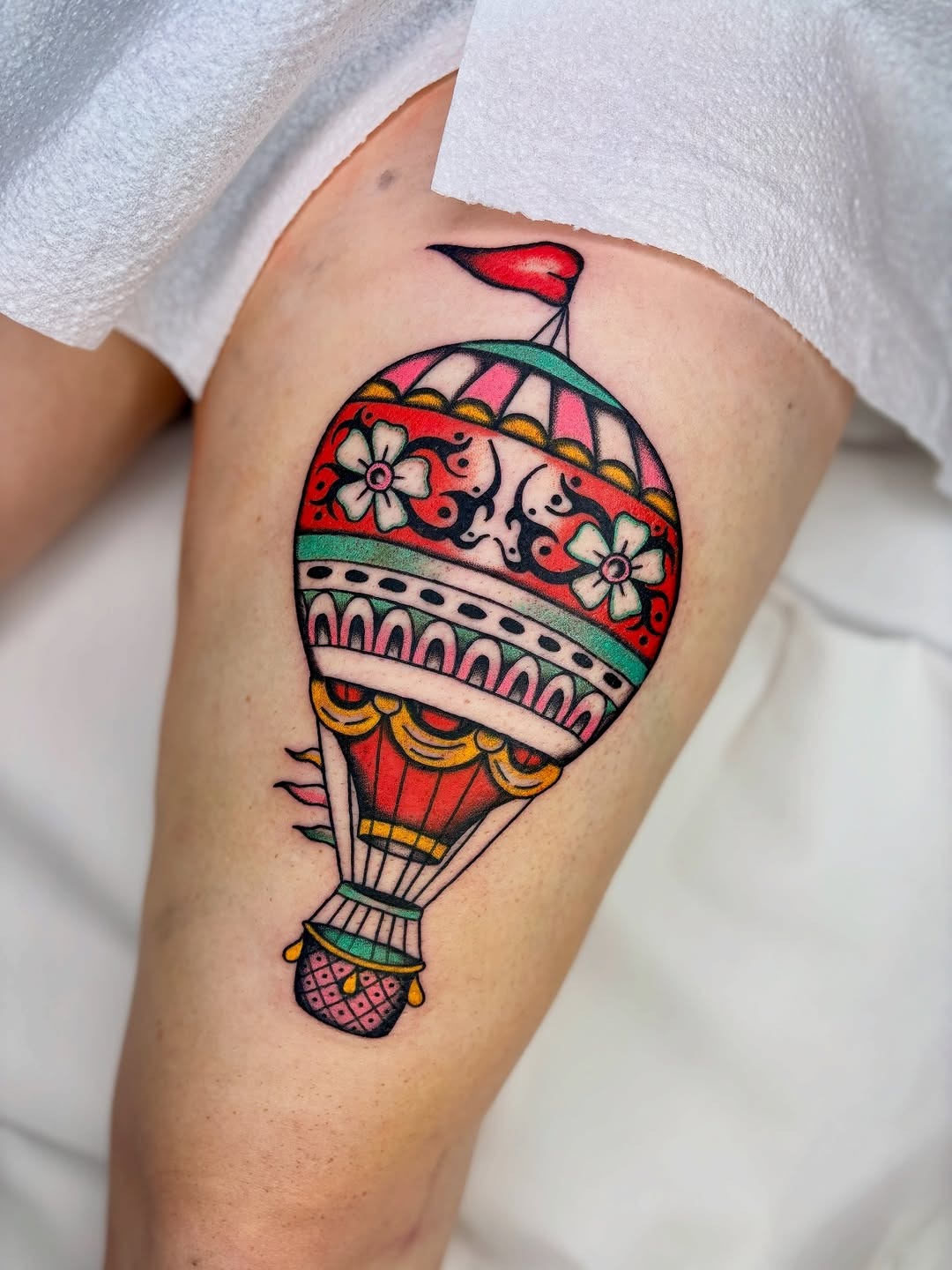 This tattoo features a bright and playful hot air balloon, adorned with intricate floral patterns and bold colors.