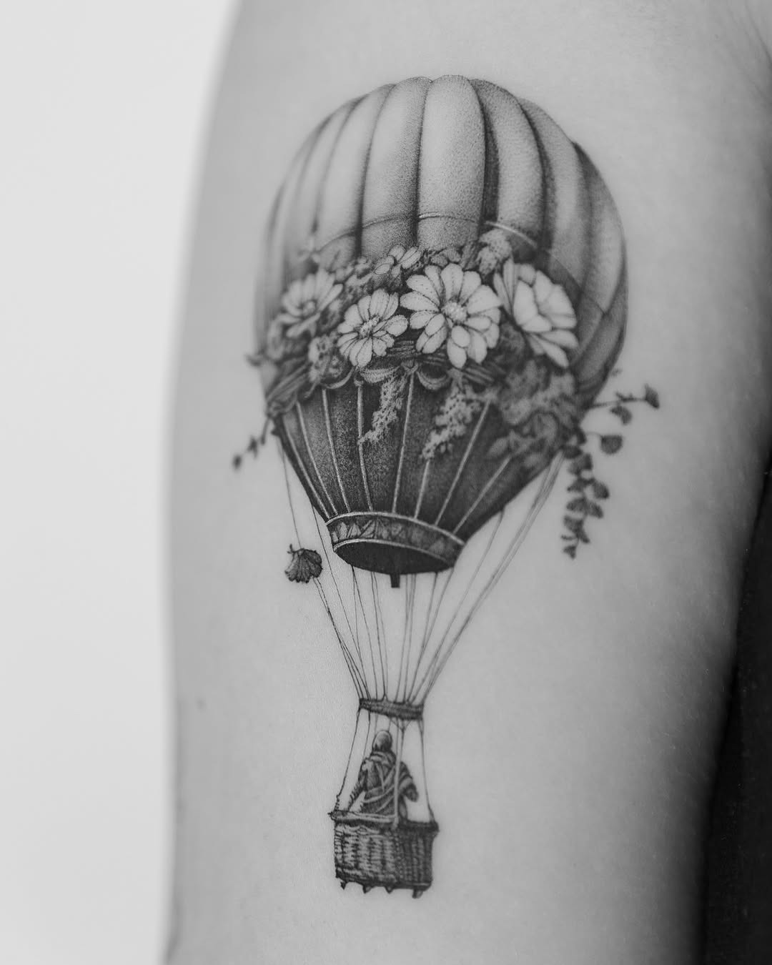 This tattoo features a beautifully detailed hot air balloon adorned with delicate flowers.