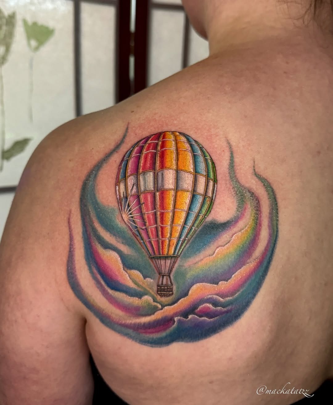 This tattoo features a beautifully detailed hot air balloon against a dreamy, colorful sky.
