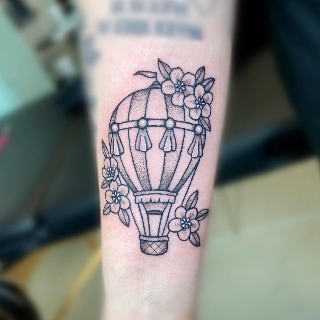 This tattoo features a beautifully detailed hot air balloon, delicately intertwined with blooming flowers.