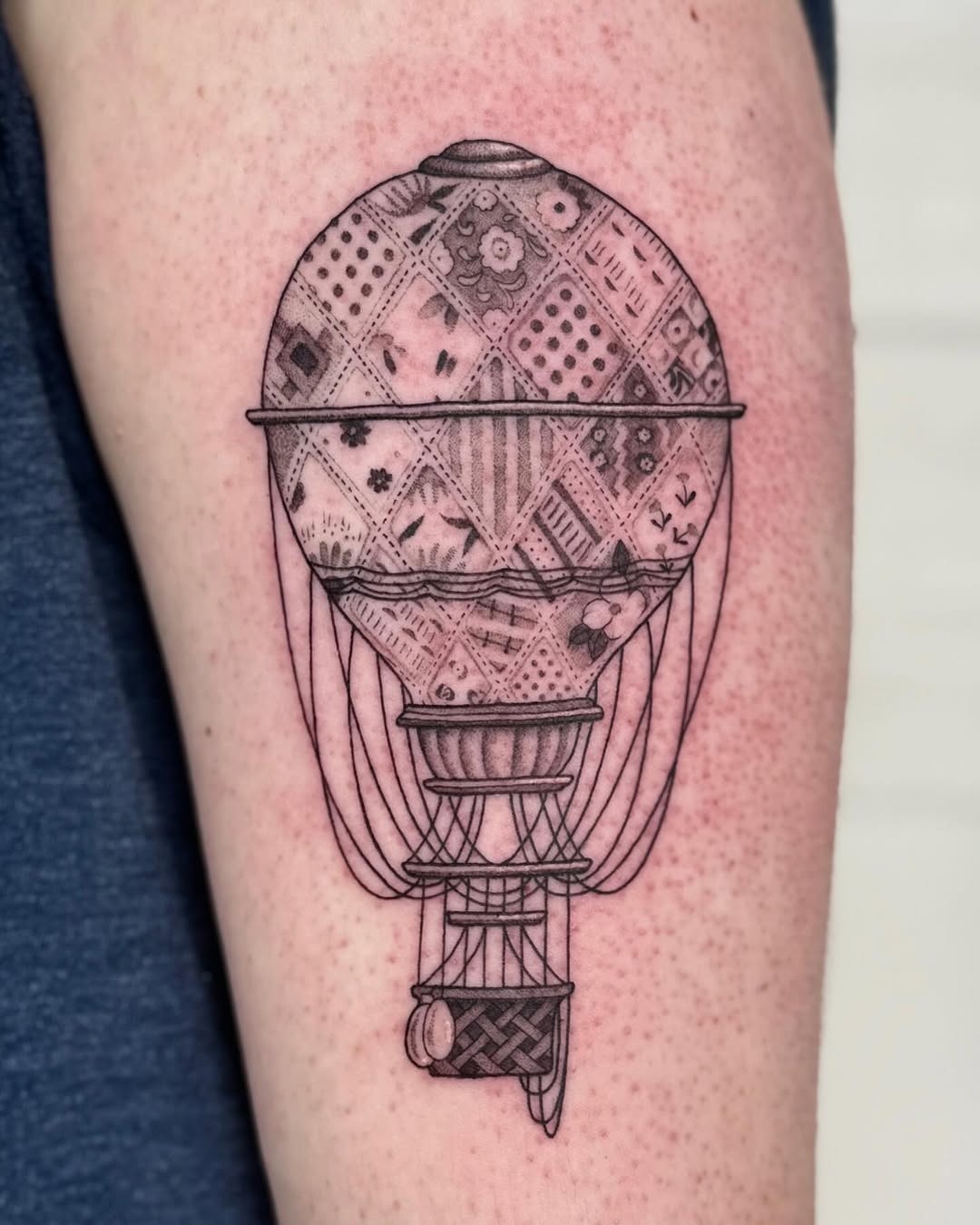This tattoo showcases a beautifully detailed hot air balloon, featuring intricate patterns that resemble fabric patches.