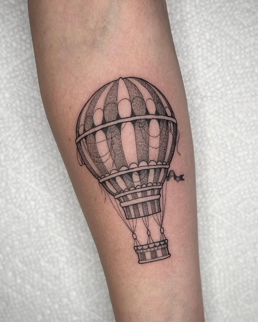 This minimalist hot air balloon tattoo features intricate line work and a delicate design.