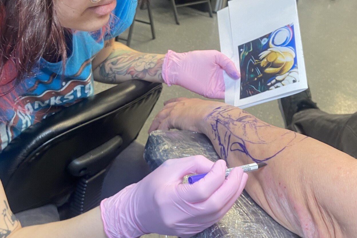 Artist making freehand adjustments to a stencil design, showing how to make tattoo stencils at home for practice