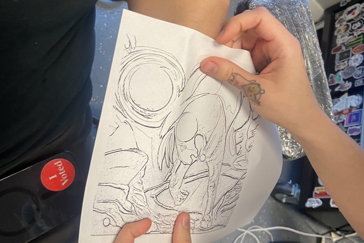 Artist checking stencil artwork size on a client's arm, showing how to use tattoo stencil paper