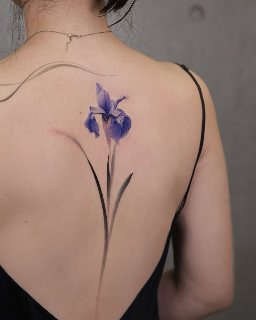 This striking iris tattoo features purple hues and delicate lines, creating a beautiful back design.