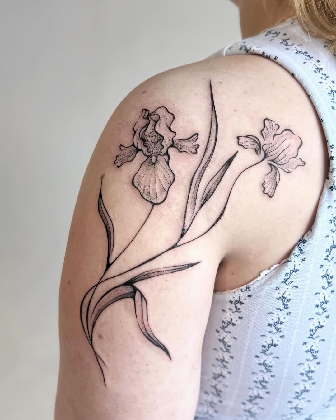 This stunning iris tattoo adorns the shoulder, showing skillful linework and delicate floral details.