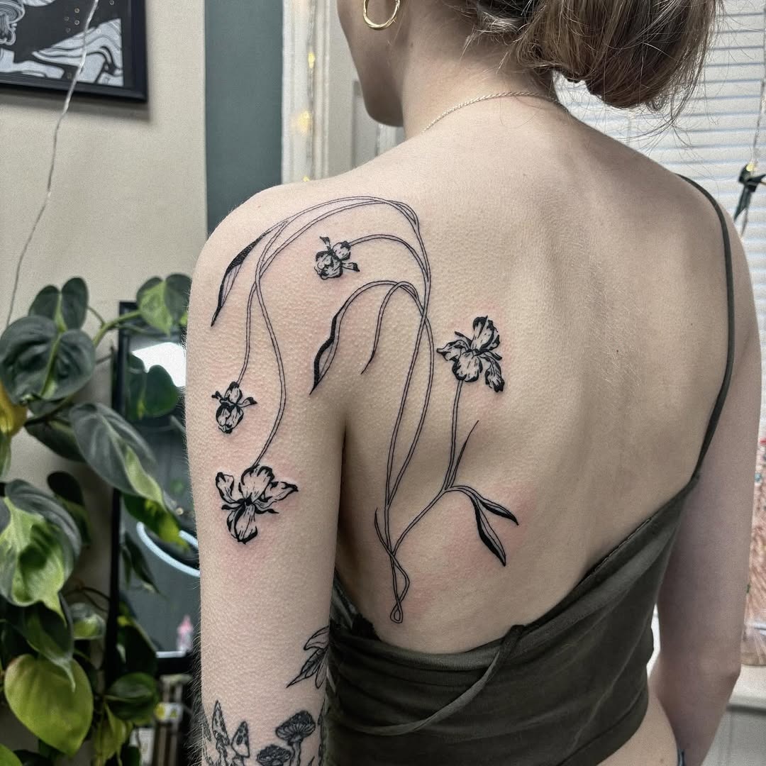 This iris tattoo elegantly sprawls across the upper back, showing delicate line work and floral details.
