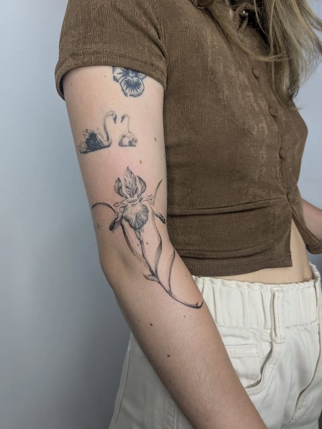 This tattoo features a beautifully detailed iris flower on the upper arm, exuding a feminine charm.