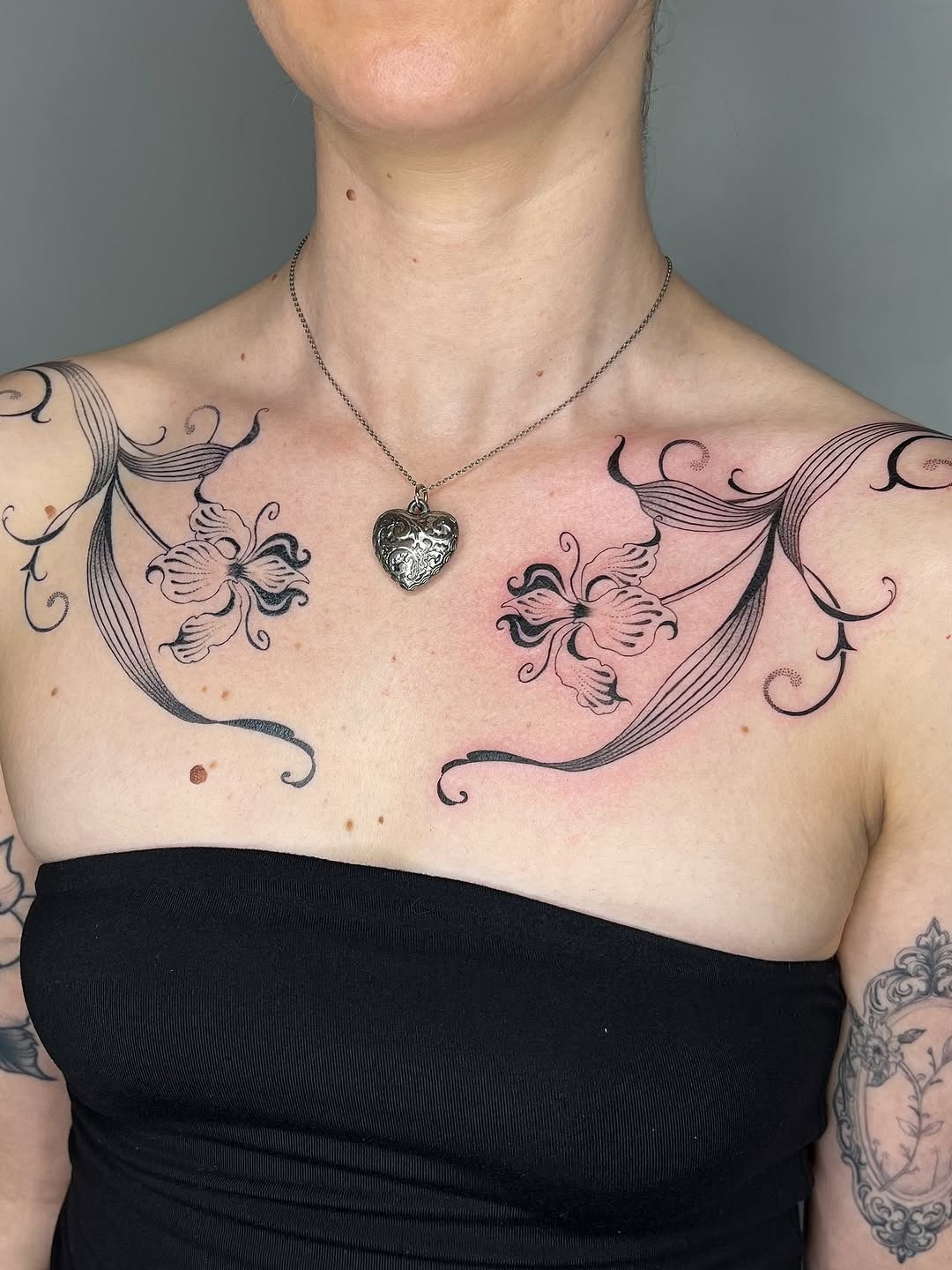 This tattoo showcases delicate irises on each shoulder, intertwined with graceful lines that flow across the skin.