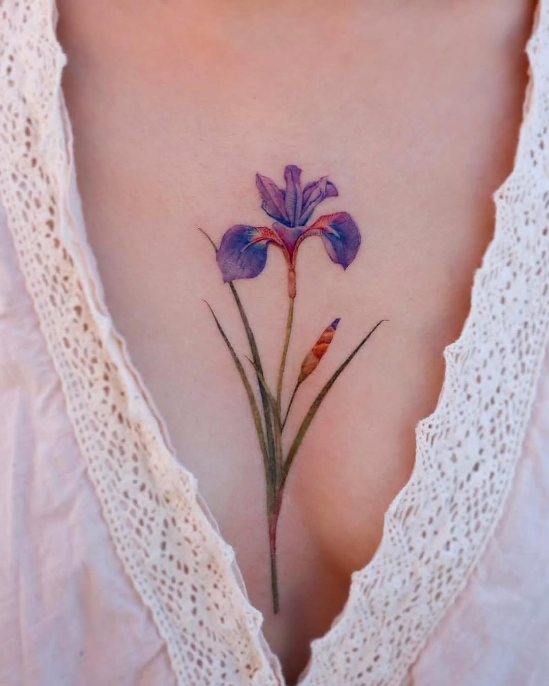 This iris tattoo features beautiful purple hues against a delicate chest backdrop.