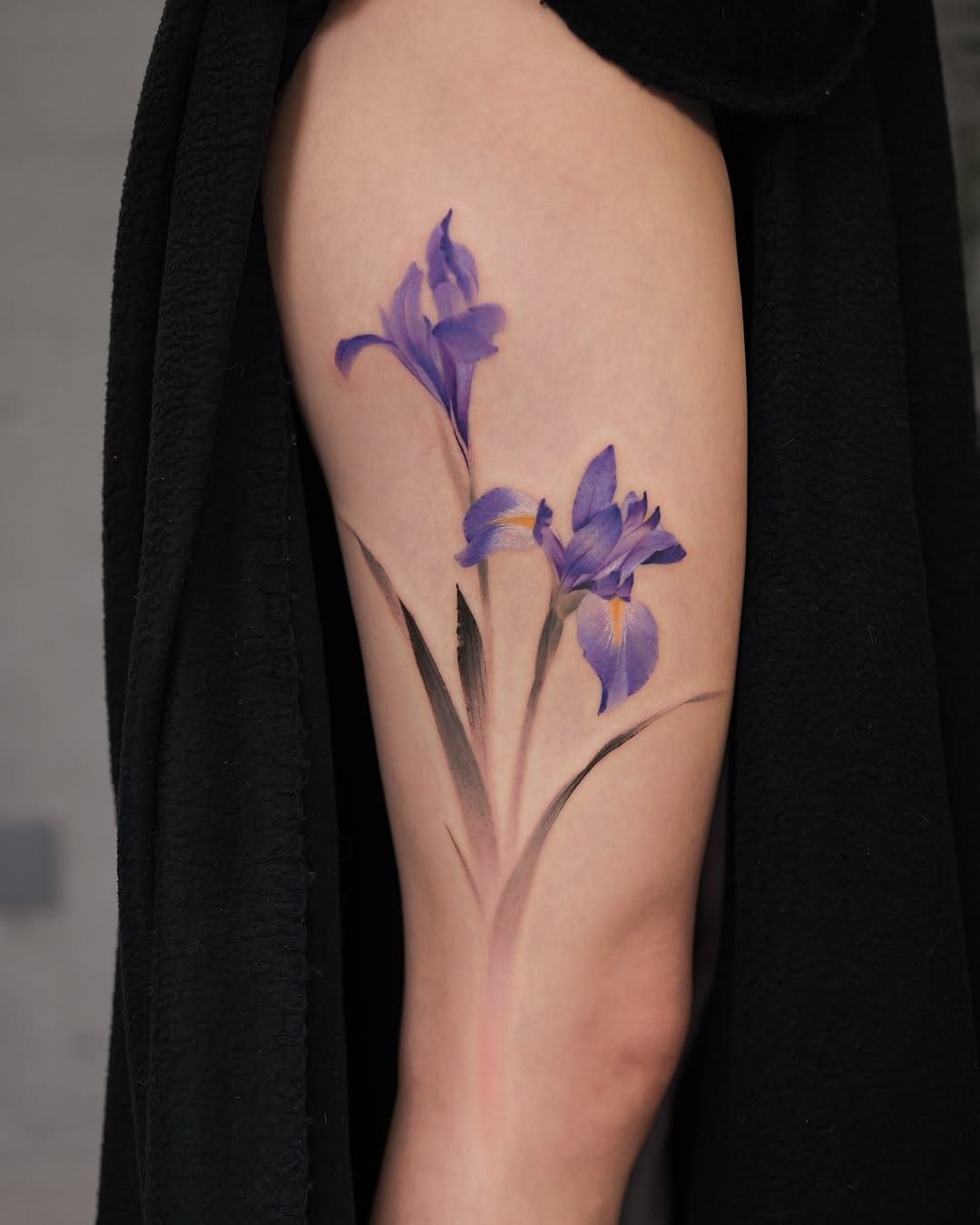This iris tattoo features purple flowers elegantly placed on the thigh.