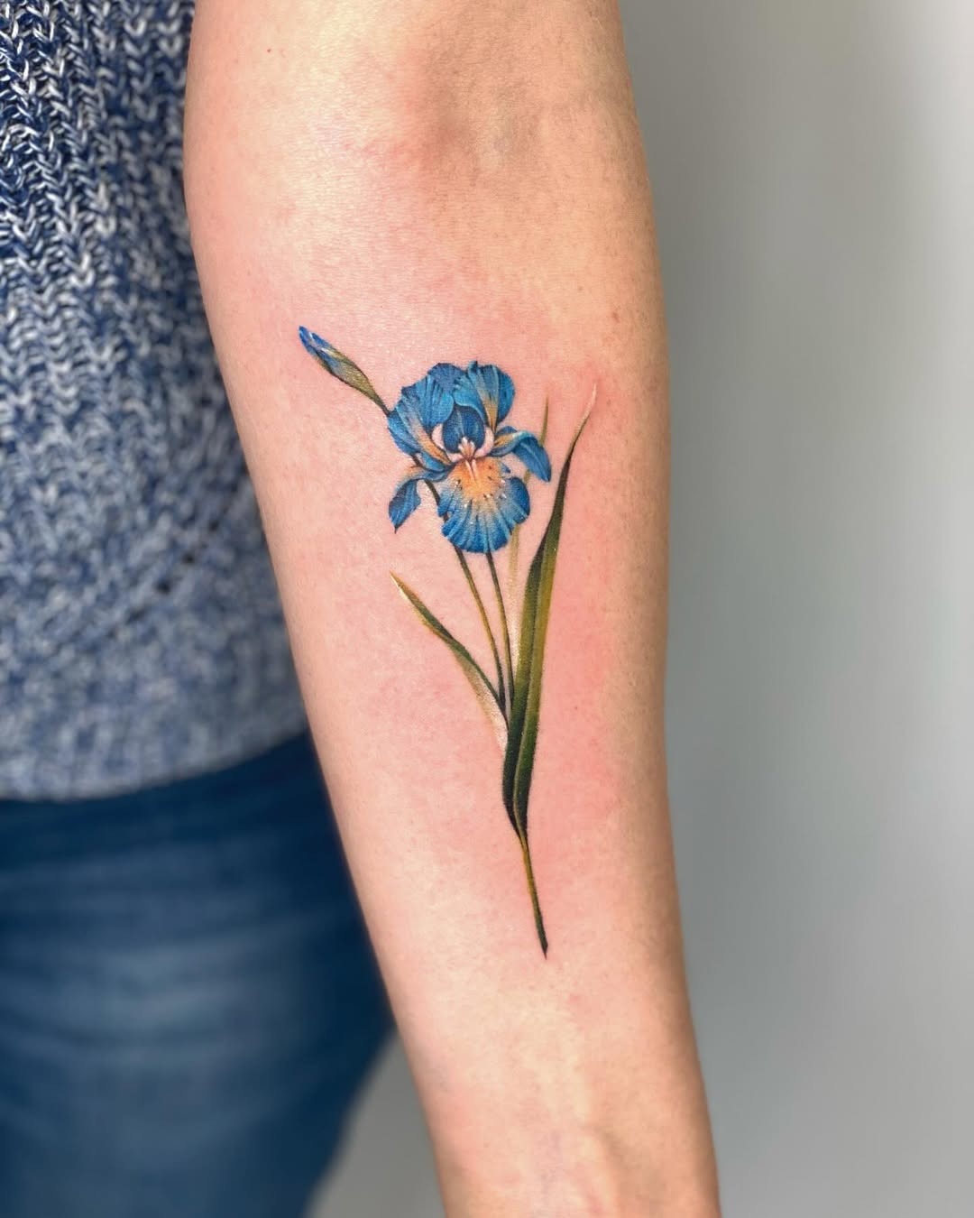 This tattoo showcases a beautiful iris flower in striking blue tones.