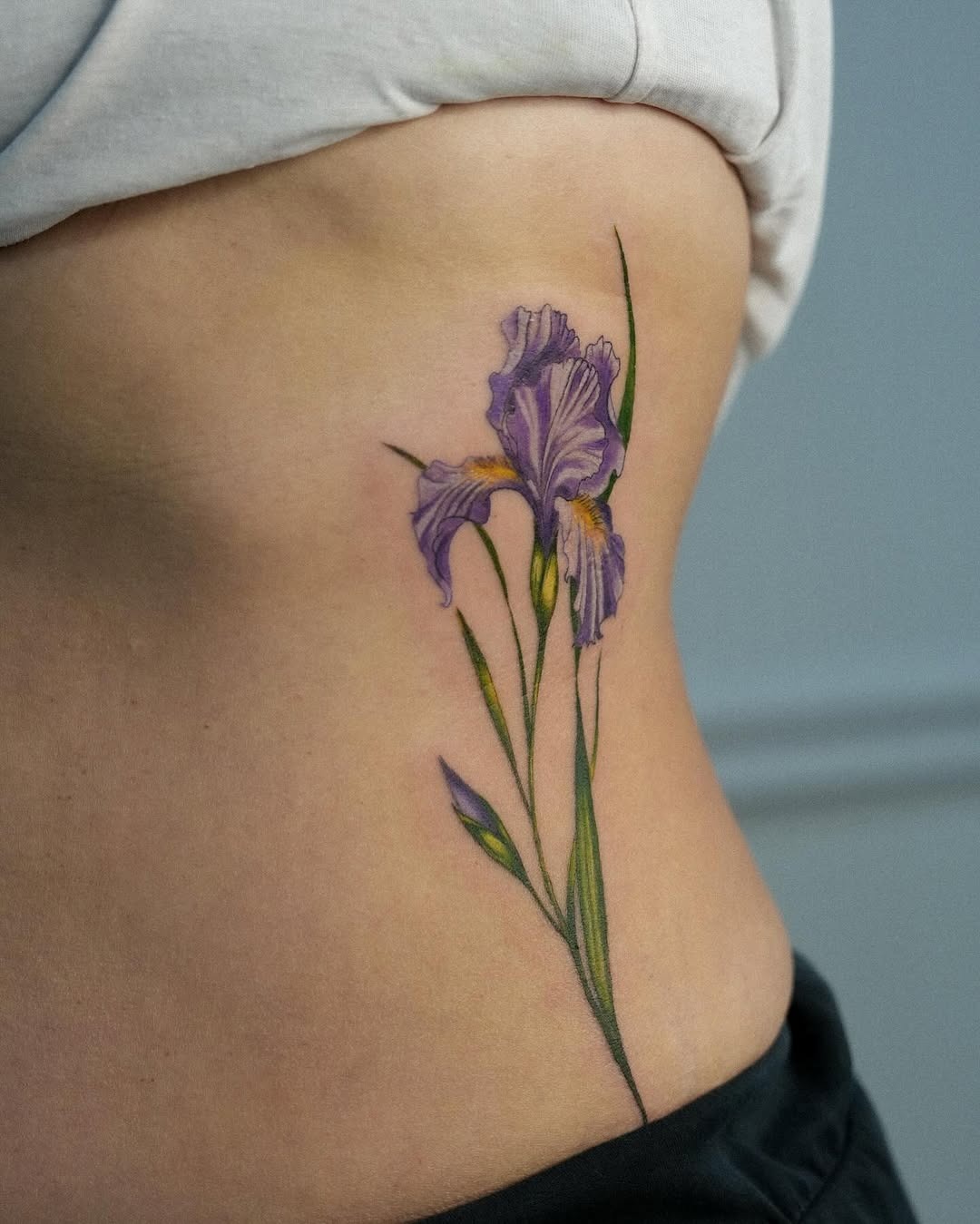 This beautiful iris tattoo features delicate purple petals and graceful green stems, resting on the side of the body.