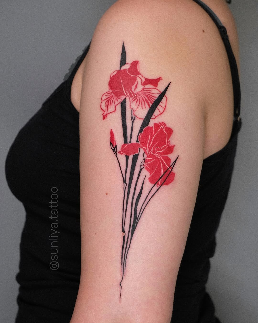 This iris tattoo features bold red flowers with striking black outlines.