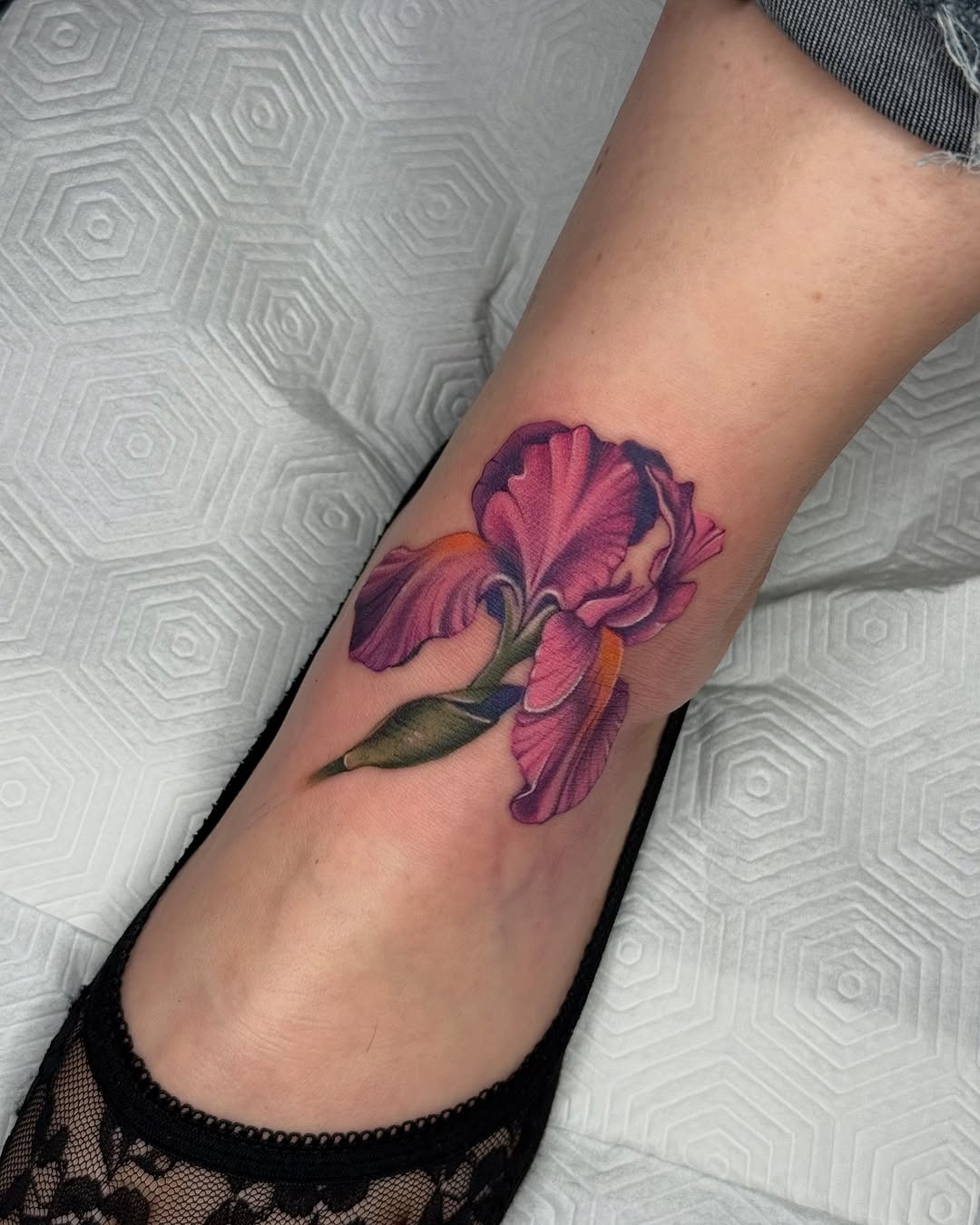 This iris tattoo beautifully adorns the ankle, showing intricate shades of purple and pink.
