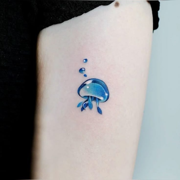 Small vivid blue jellyfish tattoo behind the wrist with glowing cyan ink accents