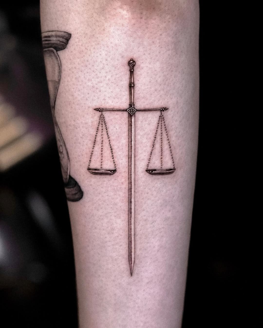 This tattoo showcases a beautifully designed sword aligned with delicate scales, representing balance and justice.