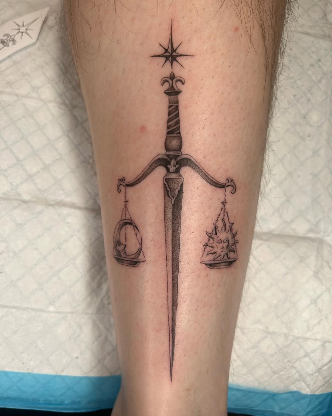 This tattoo showcases a striking sword balanced by two scales, embodying the Libra zodiac's themes of balance and justice.